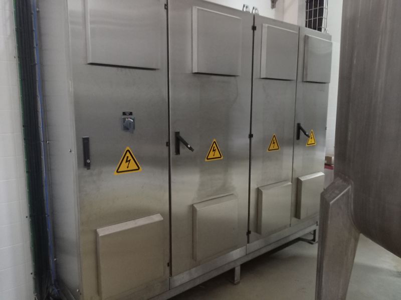 Painéis elétricos em aço inox lado a lado, com placas de advertência de eletricidade